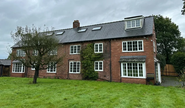Large red-brick house with a slate roof, rooflights, a dormer window and lawn