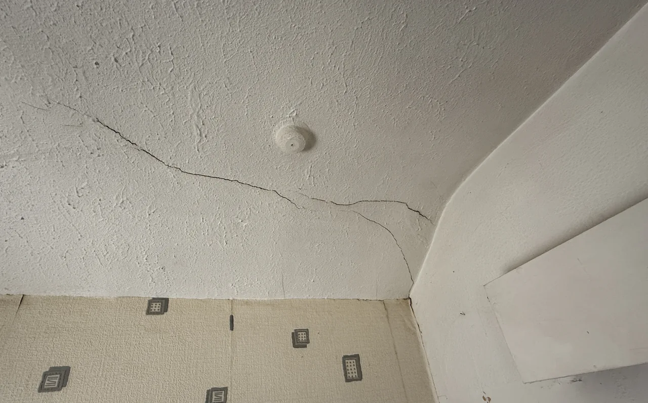 Crack across a plaster ceiling extending towards a boxed wall junction