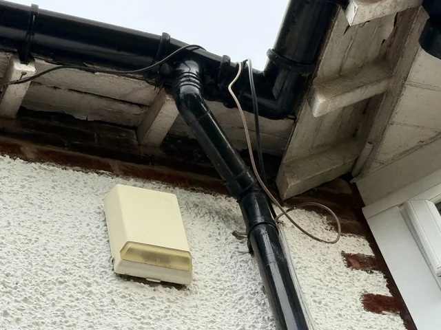 Gutter outlet and downpipe joint beside stained eaves timbers