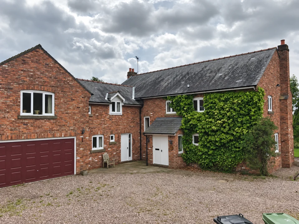 Traditional red-brick house with a slate roof, adjoining garage and a gravel courtyard