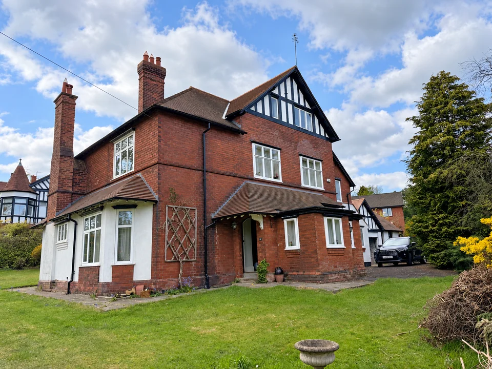 Large red-brick period house with tall chimneys, bay windows and a timbered gable