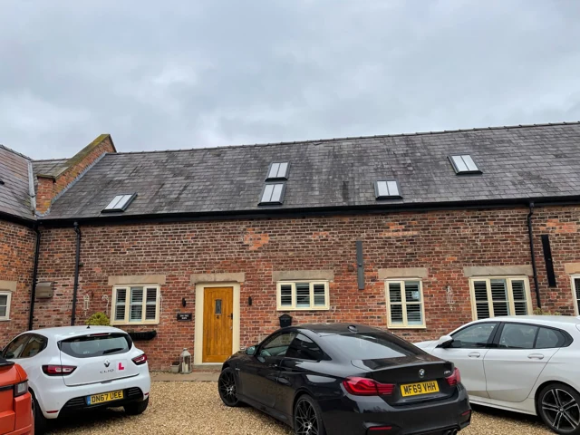 Brick-built residential property with rooflights and parked vehicles beside the entrance